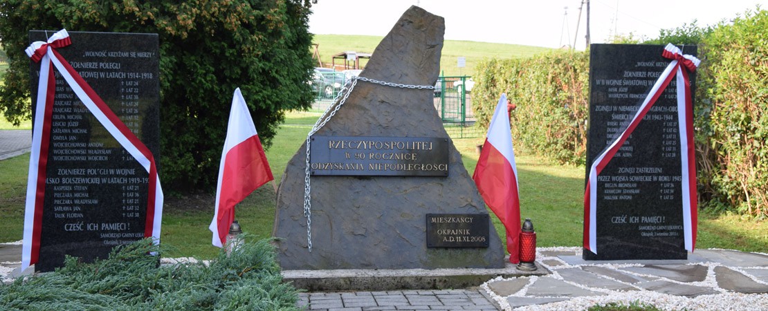 Kamienne tablice pamiątkowe w Okrajniku poświęcona rocznicy odzyskania niepodległości oraz poległym w obu wojnach światowych. Obok biało-czerwone flagi.